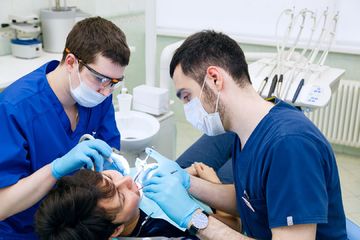 Два стоматолога лечат зубы пациента